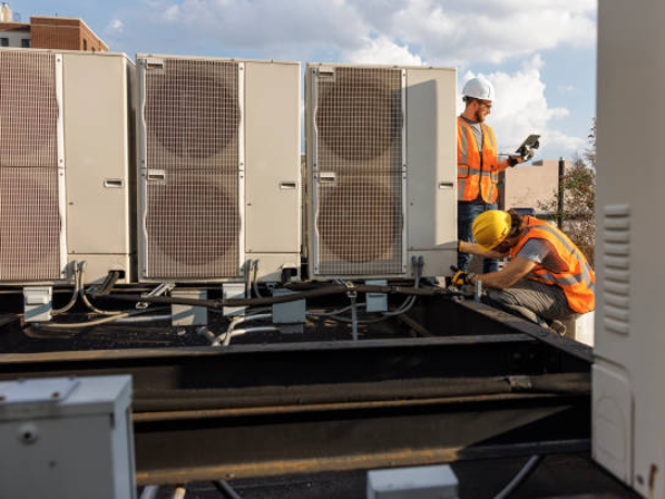 Two men working on a building with air conditioning units.